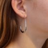 Silver oval hoop earring with sleek, modern design, shown worn on an ear.