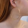 Extra large thin gold hoop earring, lightweight and waterproof, shown on a model.