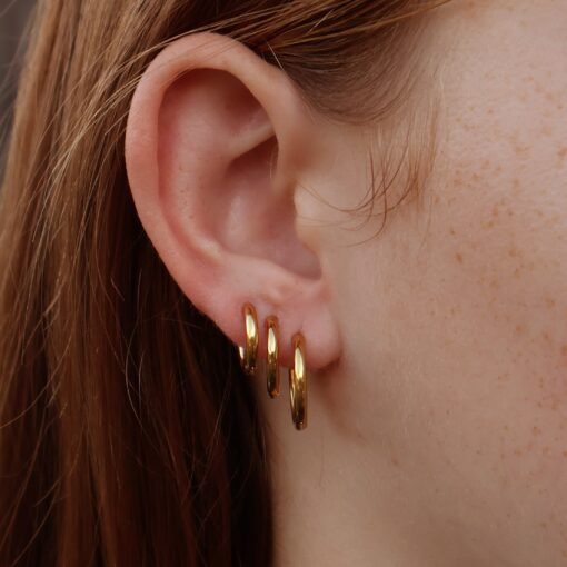 Model wearing triple-stacked gold huggie hoop earrings.