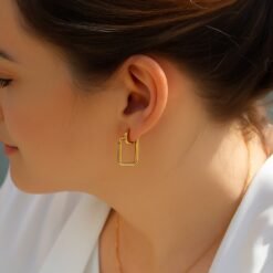 Model wearing gold huggie hoop earrings with rectangle hoop earrings.
