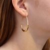 Gold oval hoop earring with sleek, modern design, shown worn on an ear.