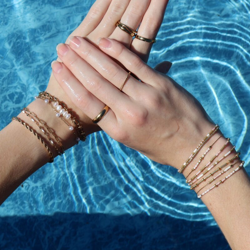 Hands displaying various waterproof and beaded rings and bracelets