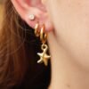 Model wearing triple-stacked gold huggie hoop earrings with starfish pendant huggies hoop earrings.