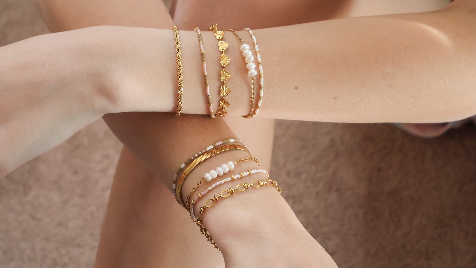 Gold & Beaded Bracelets on two wrists resting on knee.